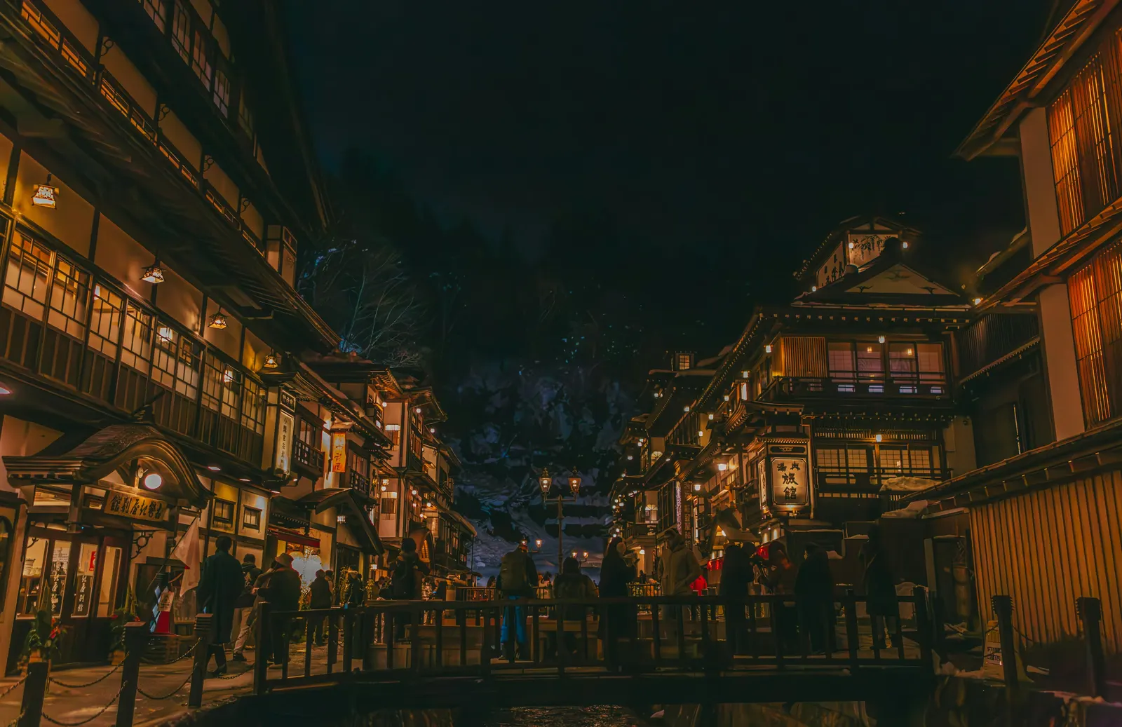 A lively onsen-town street at night, lined with traditional inns